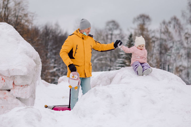 Little girl in pink walks with her dad outdoors on winter snowy day