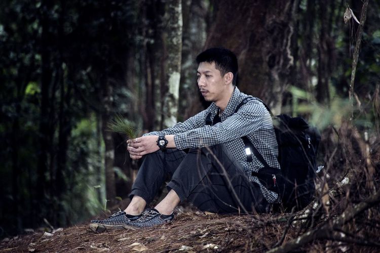 Young man sitting on tree trunk in forest