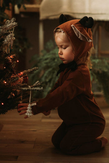 Toddler baby girl in rudolph reindeer costumes decorating christmas tree christmas tree