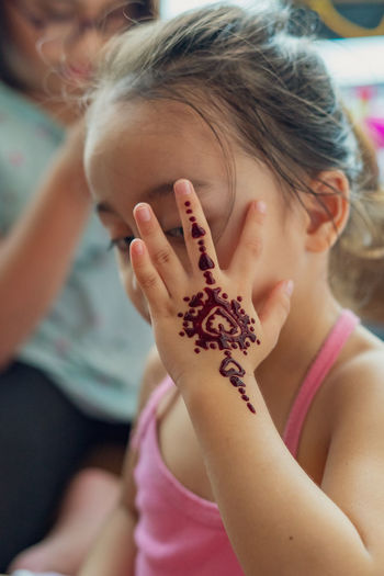 Blurry photo of henna ornaments on little girl's hand covering face.