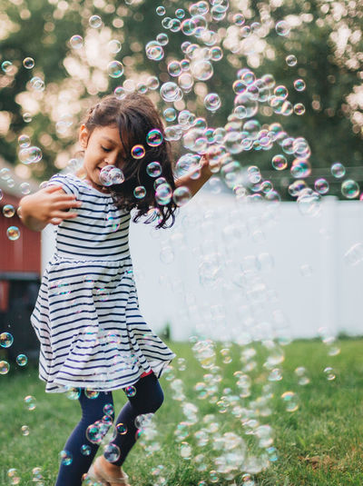 Diverse mixed race pre school age girl at home having fun playing with bubbles on a nice summer day