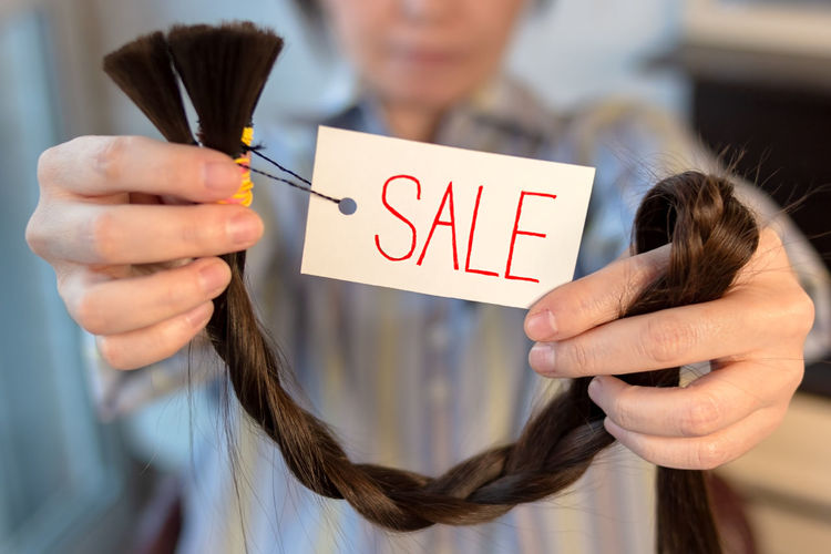 Long brown cut braid with tag in female hands, sale of woman cut hair
