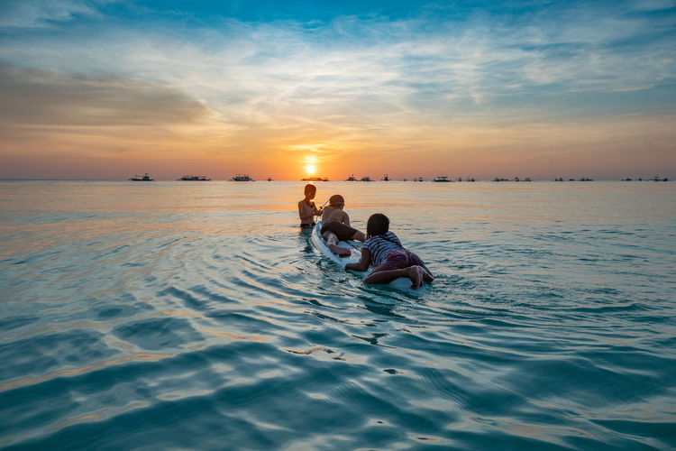 People in sea against sky during sunset
