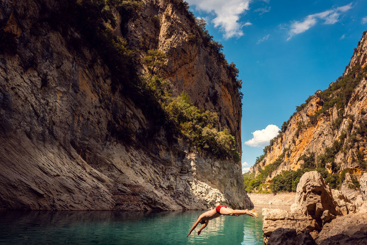 Man jumping into the water of a gorge in the pyrenees mountains on a hot day