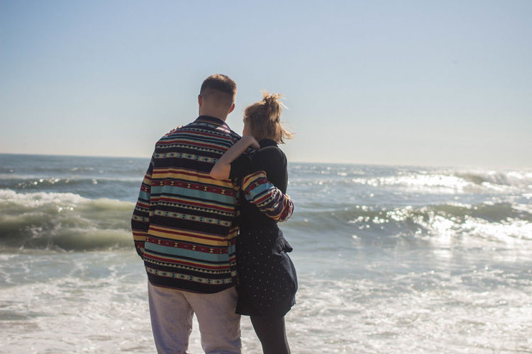 Couple embracing while standing at beach against sky