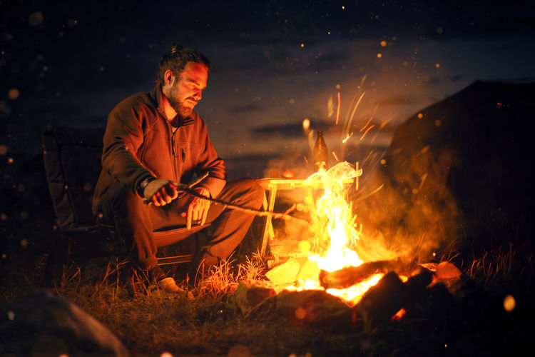 Man sitting on chair by campfire at night