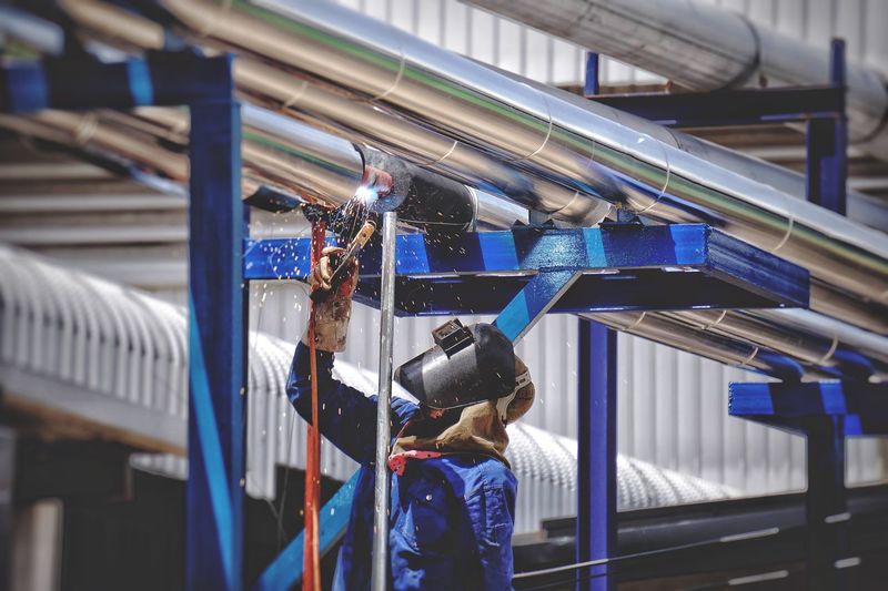 Male worker welding pipes at factory