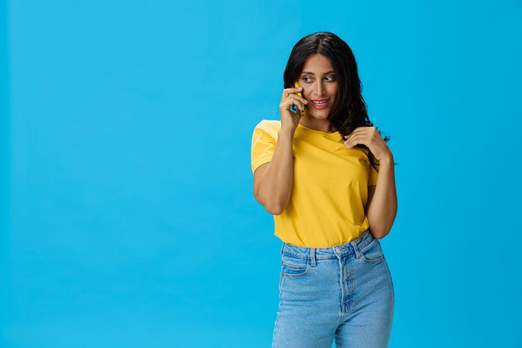 Young woman looking away while standing against blue background
