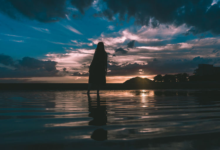 Silhouette man standing on sea against sky during sunset