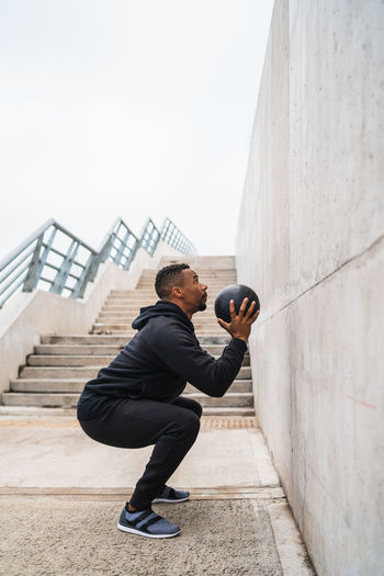 Full length of man exercising outdoors with medicine ball against wall