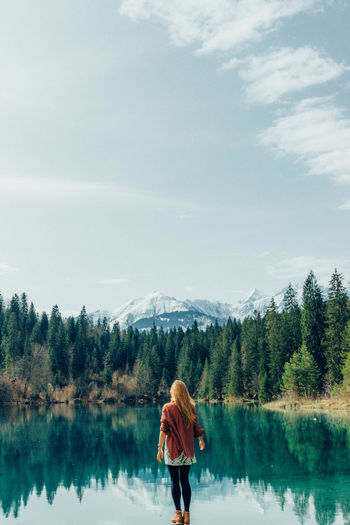 Rear view of woman standing by idyllic lake