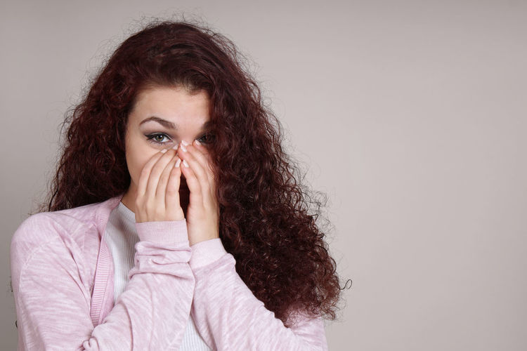 Portrait of young woman covering face against beige background