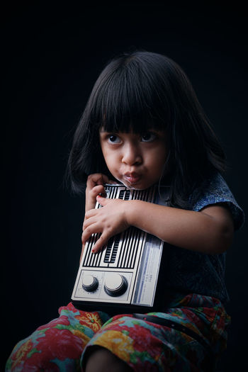 Portrait of cute girl holding radio against black background