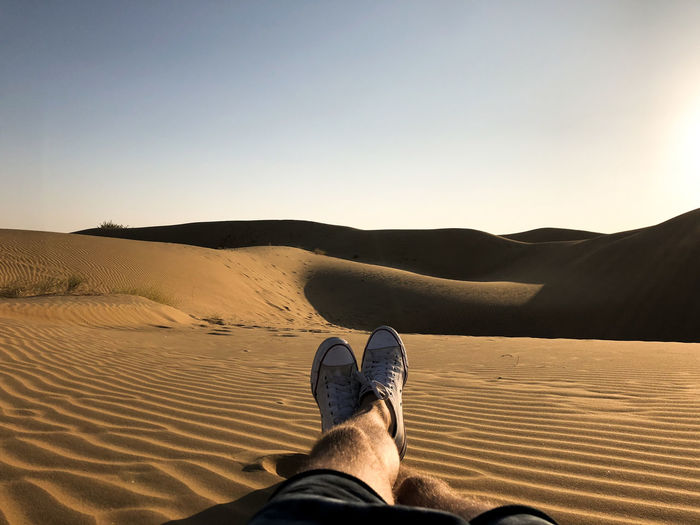 Low section of man resting on sand at desert