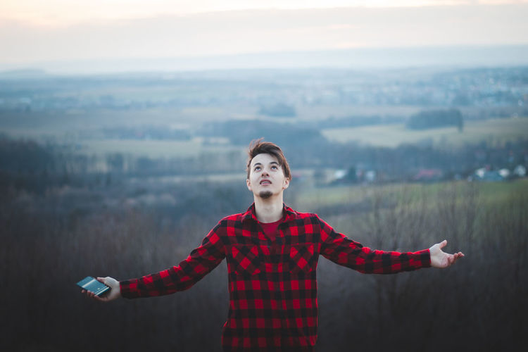 Candid portrait of a man in his 20s dressed in a black and red checked shirt joyfully facing the sky
