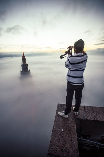 Rear view of man photographing palace amidst clouds at sunset
