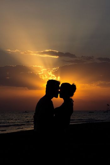 Silhouette couple romancing at beach against sky during sunset