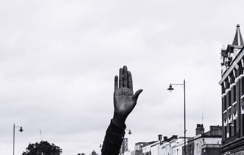 Cropped hand against sky in city
