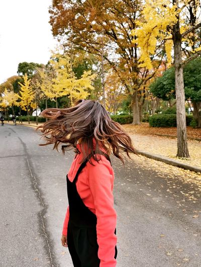 Woman tossing hair while standing on road during autumn