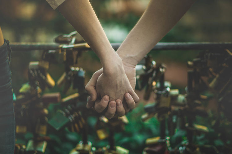 Cropped image of couple holding hands against padlocks on railing