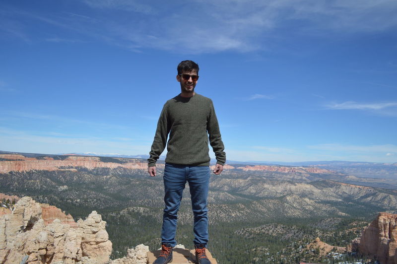 Full length portrait of young man standing on rock against sky