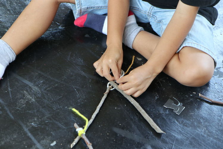 Low section of person tying sticks while sitting on floor