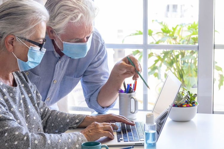 Senior couple wearing flu mask using laptop at home