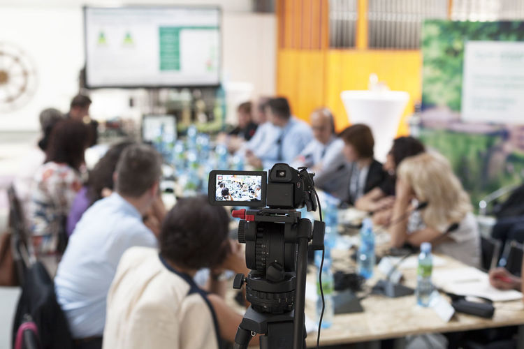Video camera on tripod filming business meeting in board room during conference