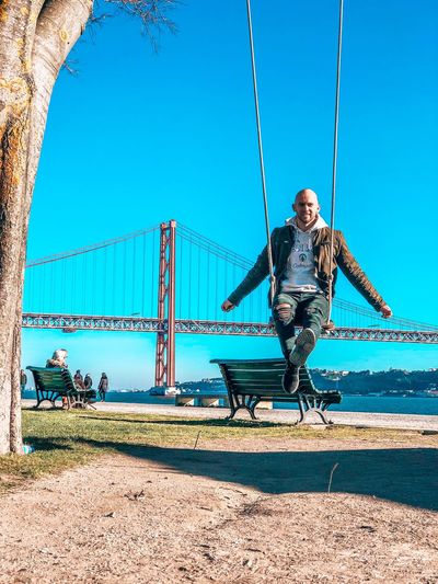 Man sitting on swing against clear sky