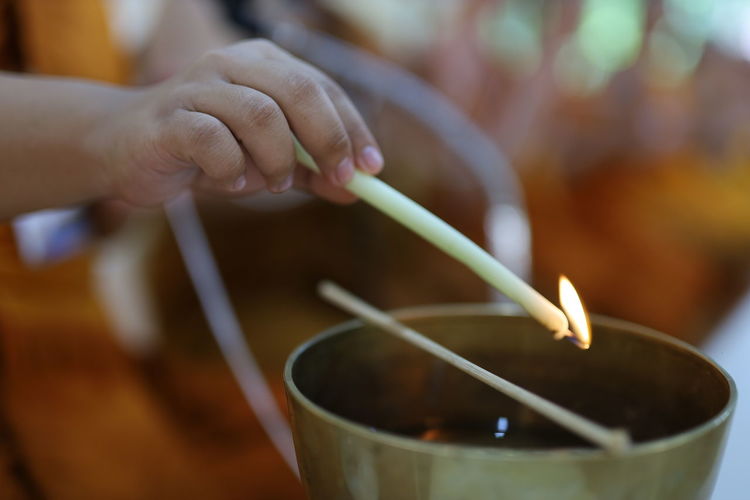 Close-up of buddhist novice monk hands lighting butter lamp with candle in temple