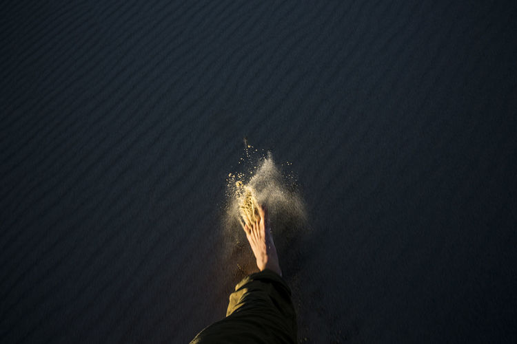 A foot kicks up sand into the light from shadow.