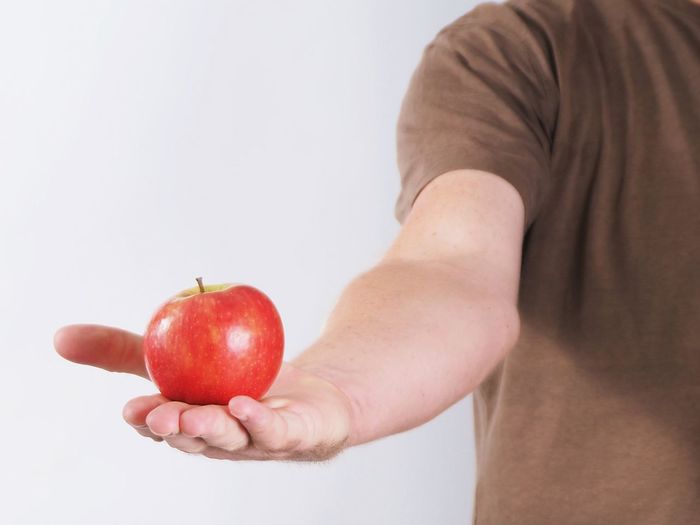 Close-up of hand holding apple against white background