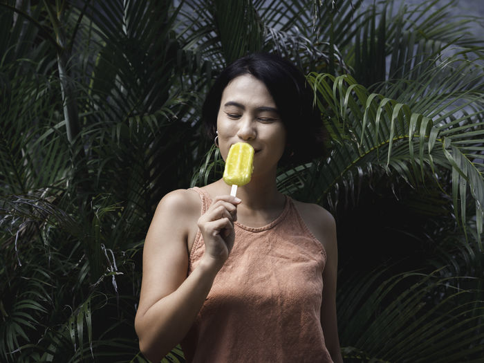Happy smile asian woman short hair holding yellow popsicle on green leaves background.