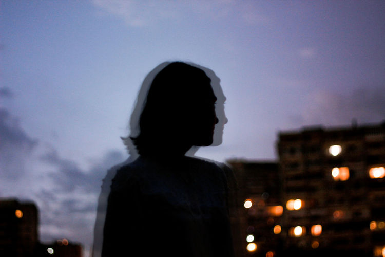 Rear view of silhouette woman in illuminated city against sky