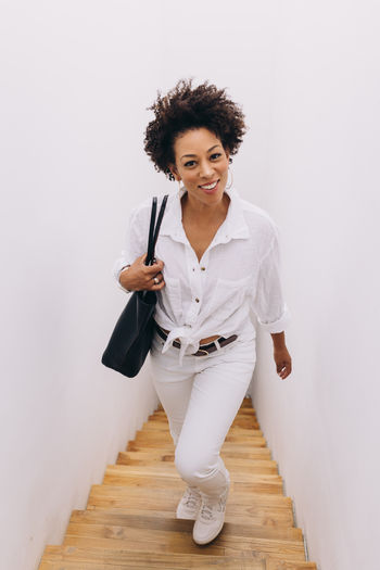 Black woman dressed in white carrying a bag, walking up the stairs