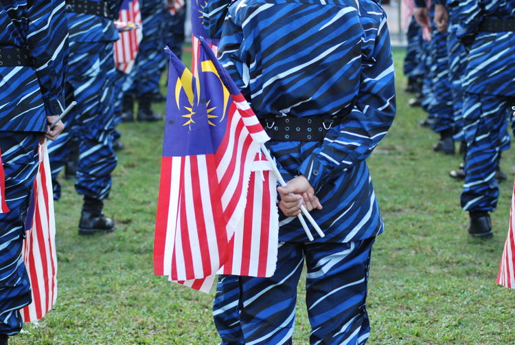 Rear view of people with malaysian flags on grassy field during celebration