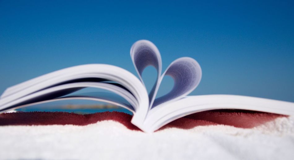 Book pages forming heart shape on towel against clear blue sky