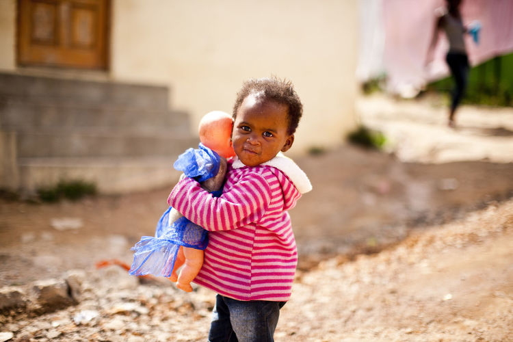 Portrait of boy with doll on footpath in town