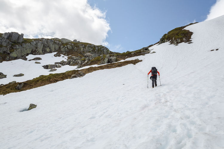 Rear view of hiker with poles on mountain against sky