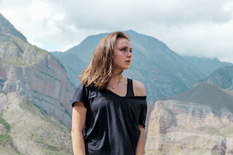 Beautiful young woman looking away while standing against mountain range