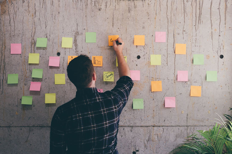 Rear view of man writing on adhesive note in office