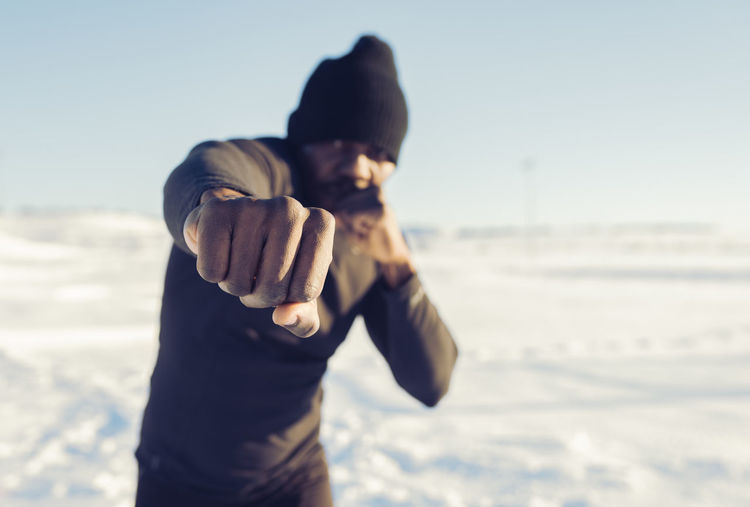 Mid adult sportsman punching while exercising in snow during sunny day
