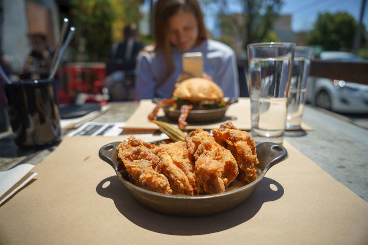 Woman sitting by burger and fried food served on table