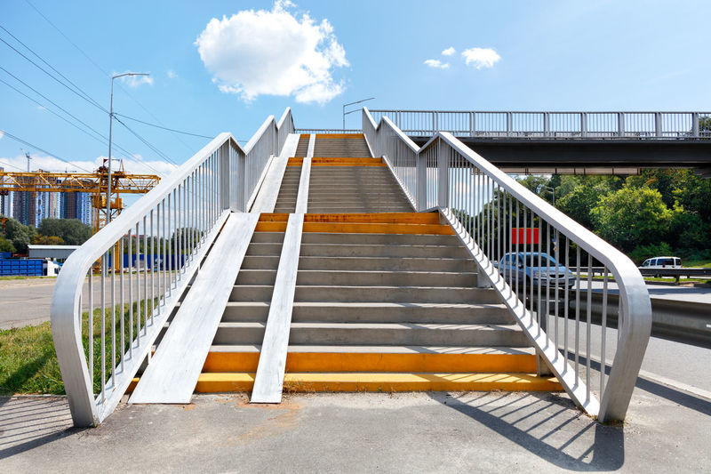 A staircase going up to a pedestrian bridge, an overpass and a crossing over  highway on sunny day .