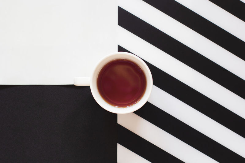 Cup of coffee / tea on black and white table with stripes in minimal style. top view, flat lay