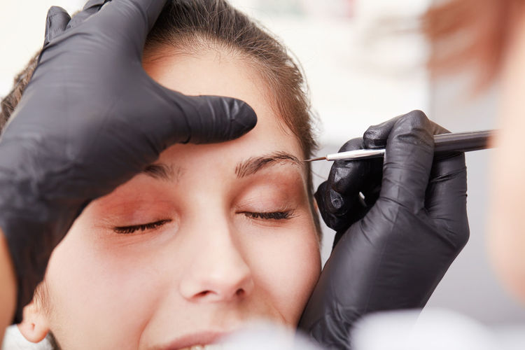 Cropped hands of beautician treating woman permanent eyebrow