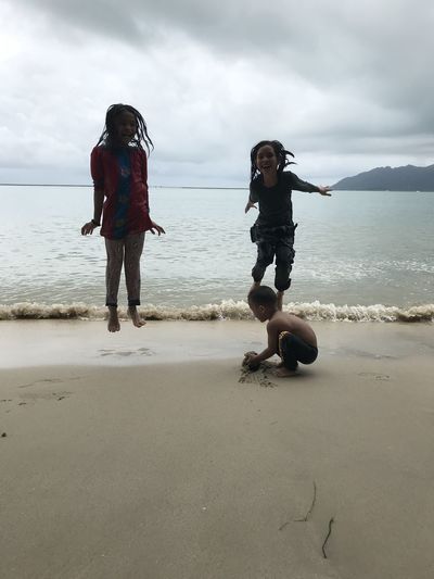 Siblings enjoying at beach against cloudy sky
