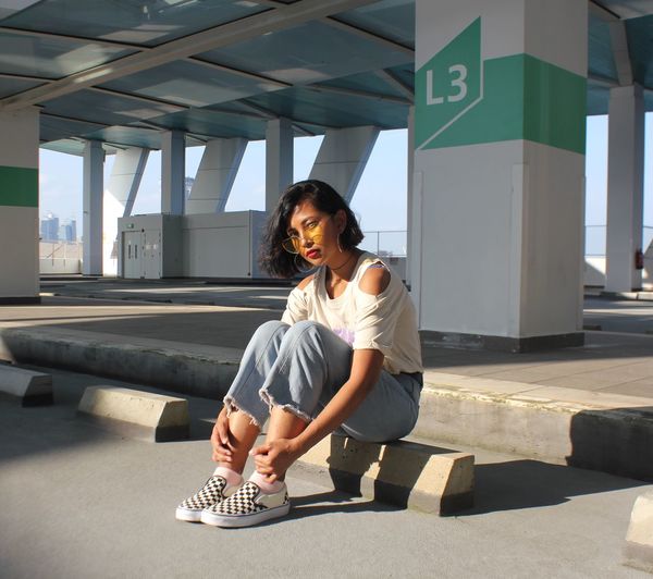 Full length portrait of young woman sitting on road