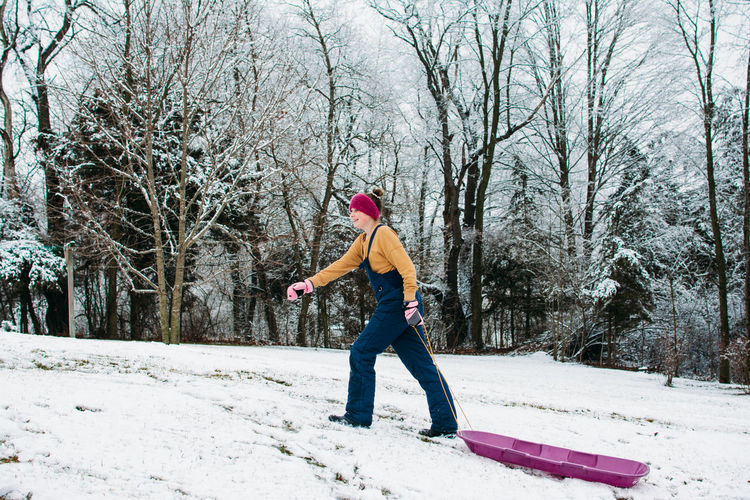 Girl walking up a snowy hill pulling a sled