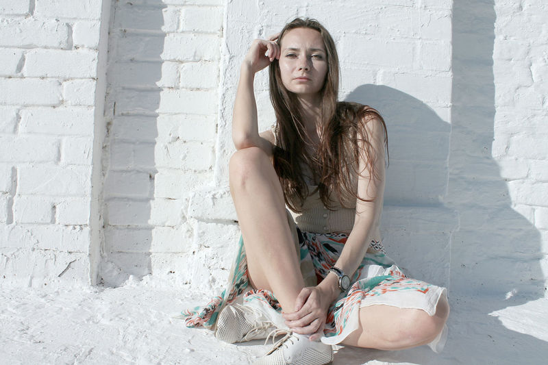 Full length portrait of woman sitting against wall during sunny day